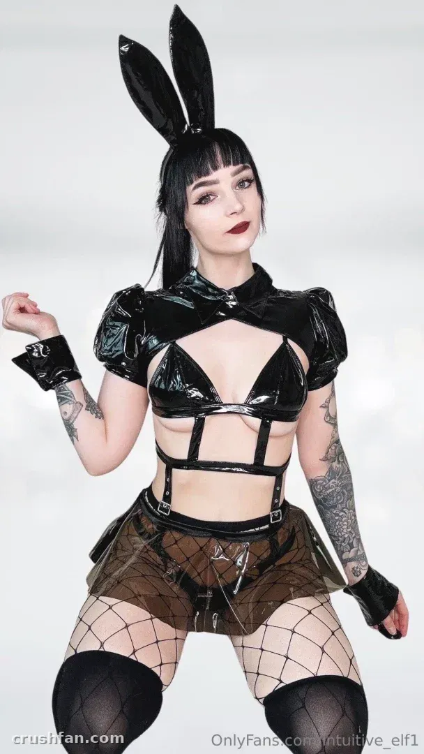 That Elf Lady in einem glänzenden schwarzen Outfit mit Hasenohren und Fischnetzstrumpfhosen vor einem weißen Hintergrund.
