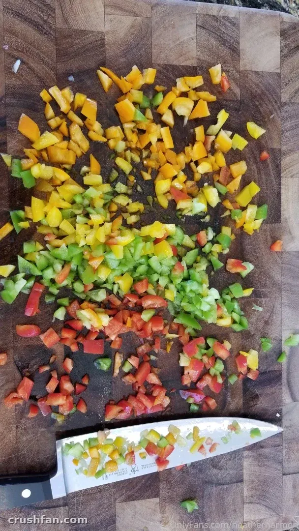 Pimientos amarillos, verdes y rojos picados sobre una tabla de madera con un cuchillo de chef