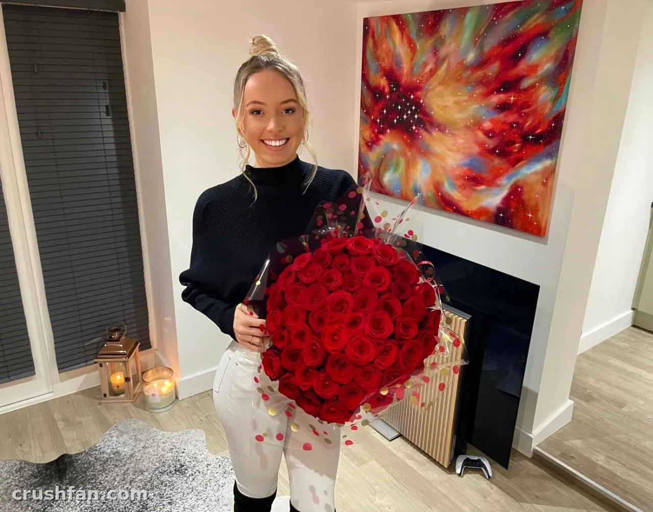 Mistress Cardi hält drinnen neben einem Kamin einen großen Strauß roter Rosen.