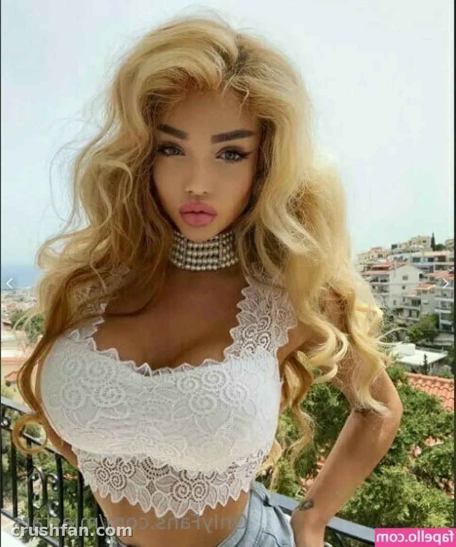 Mia in a white lace crop top and glittering choker on a sunny balcony with town buildings behind her