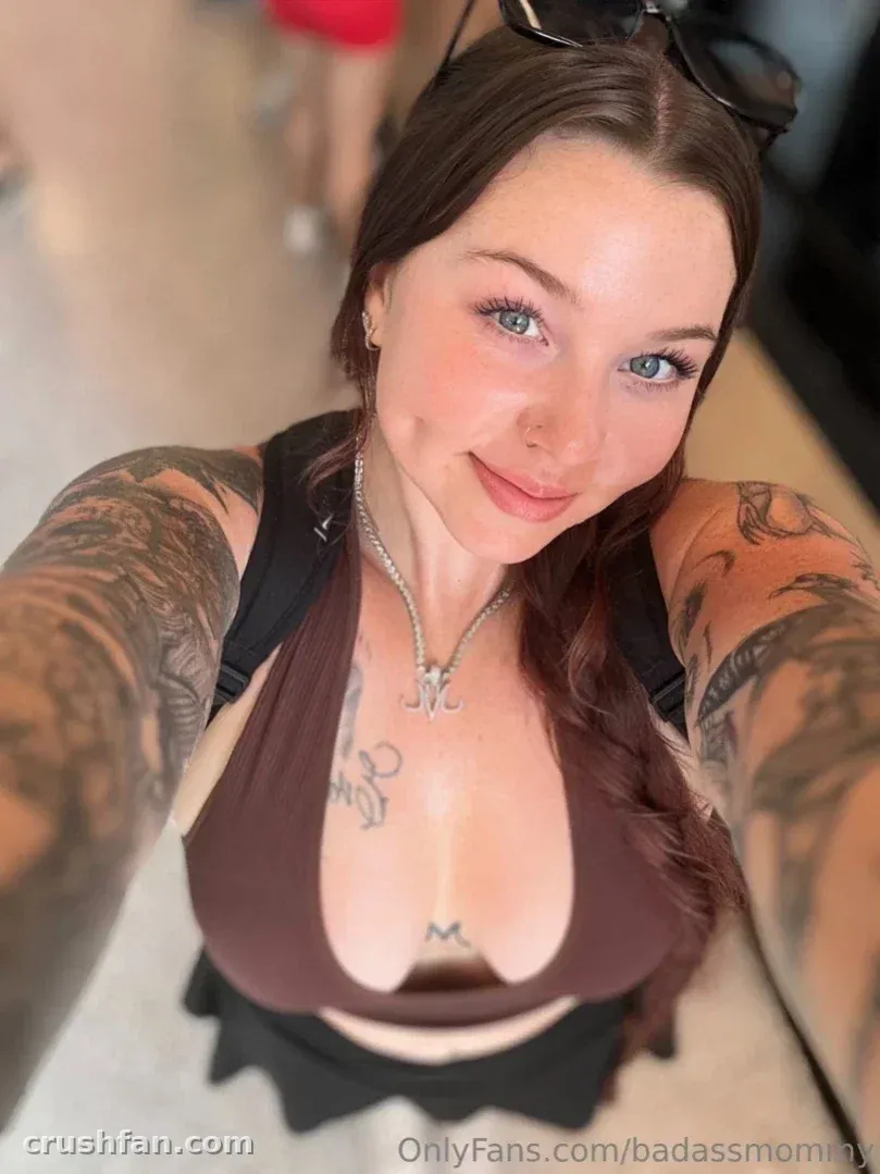 Sara con un top halter marrón y tatuajes, tomándose una selfie en interiores.