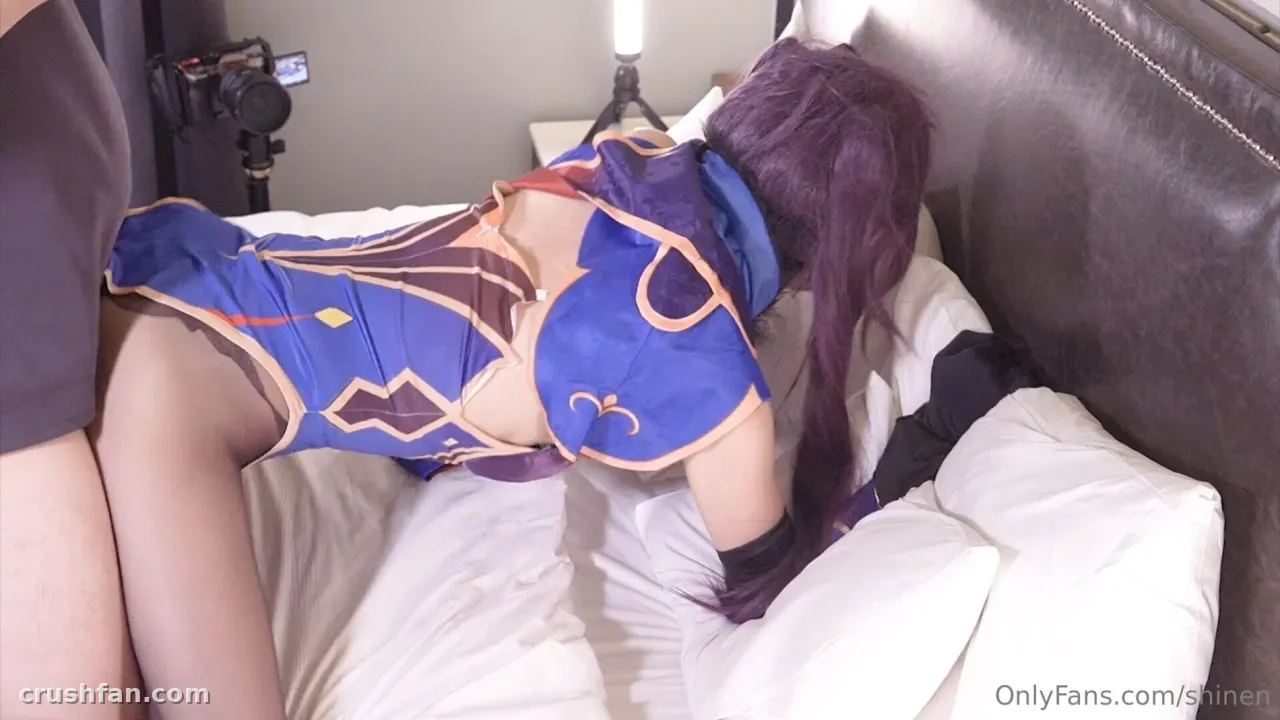 Haru dans un costume bleu et doré allongée sur un lit blanc avec du matériel photo à proximité