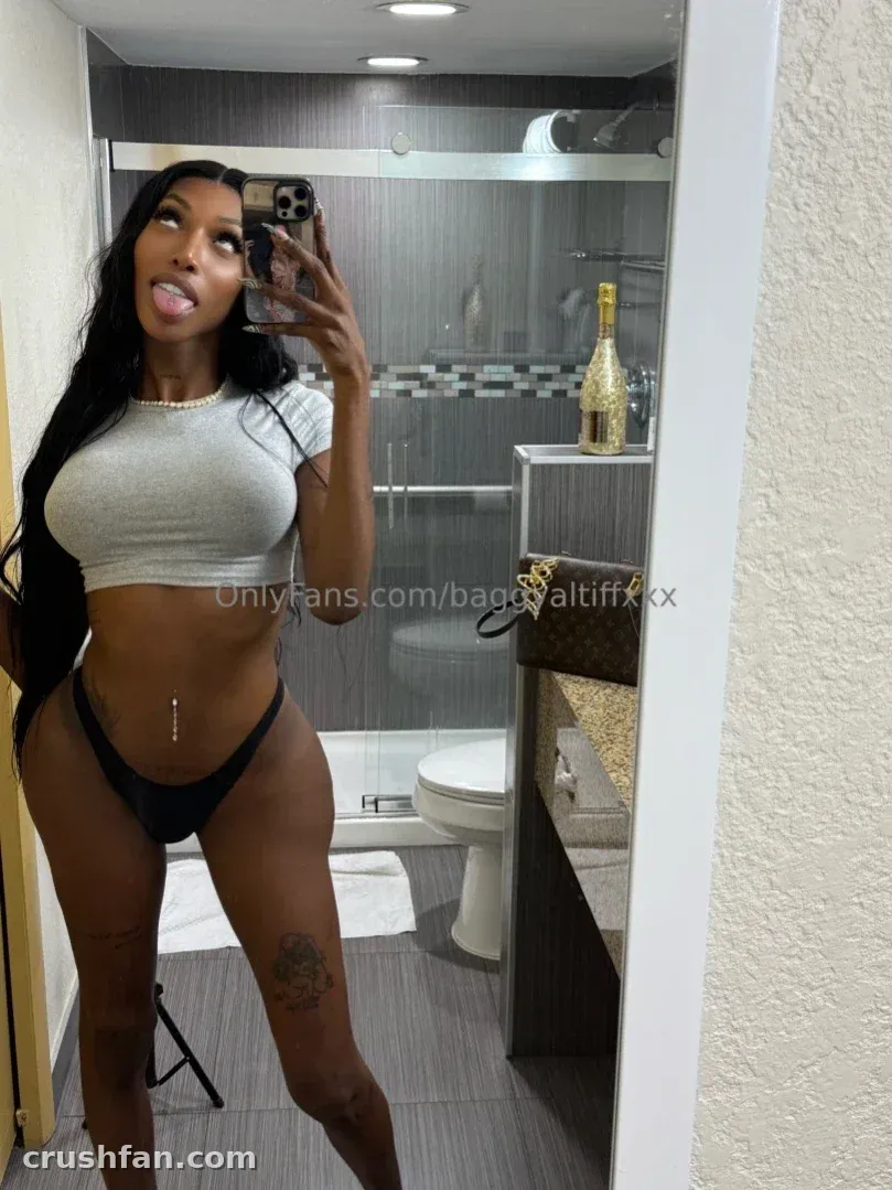 mAmi-Tiff prenant un selfie miroir dans une salle de bain, portant un crop top blanc et une culotte de bikini noire.
