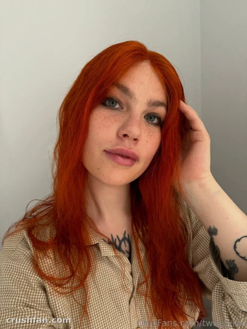 Laura with long red hair in a beige check shirt against a plain grey wall
