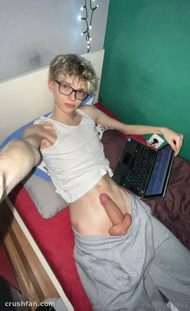 Horváth Ádám de regata branca e calça de moletom cinza tirando uma selfie em uma cama com um laptop.