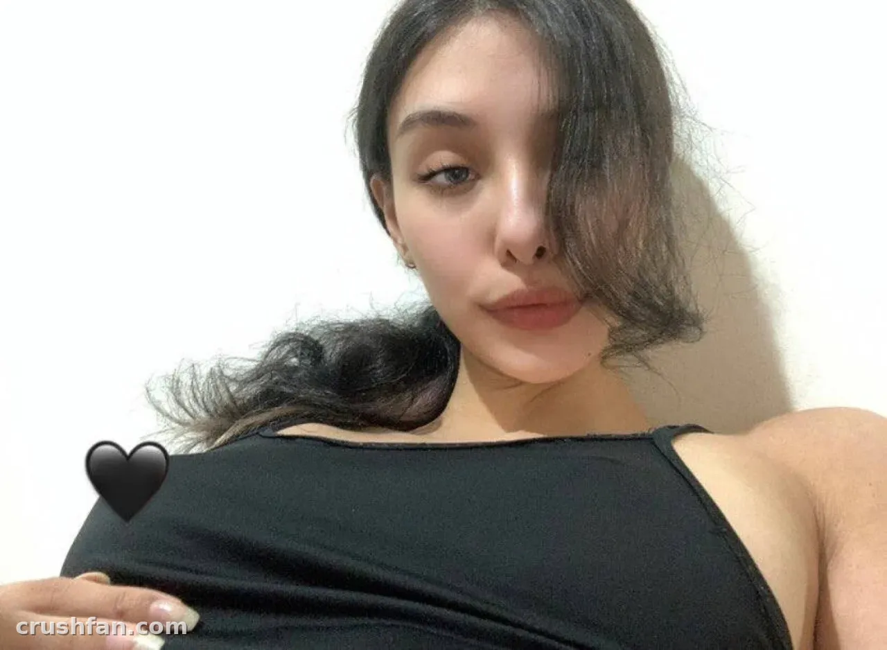 Creator in a black top against a white wall, hair falling across her face