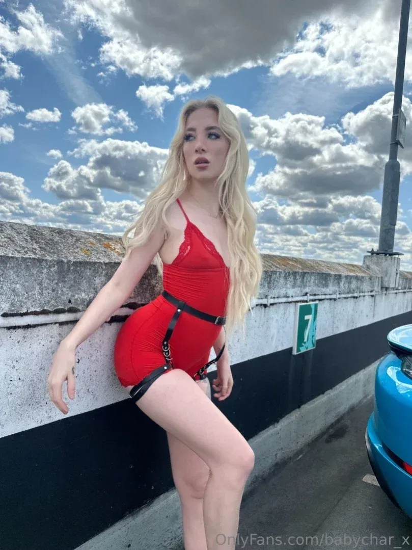 Charlotte in a red bodysuit leaning on a wall under a cloudy sky