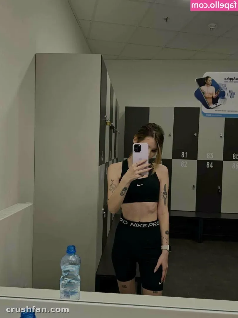 Anicka in a black sports bra and shorts taking a mirror selfie in a locker room