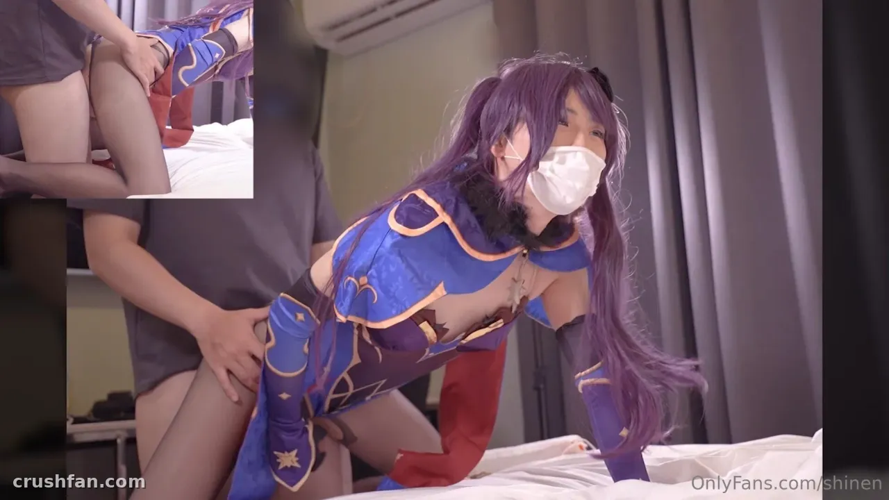 Haru in einer lila Perücke und einem blauen Cosplay-Outfit, kniend auf einem Bett in Innenräumen