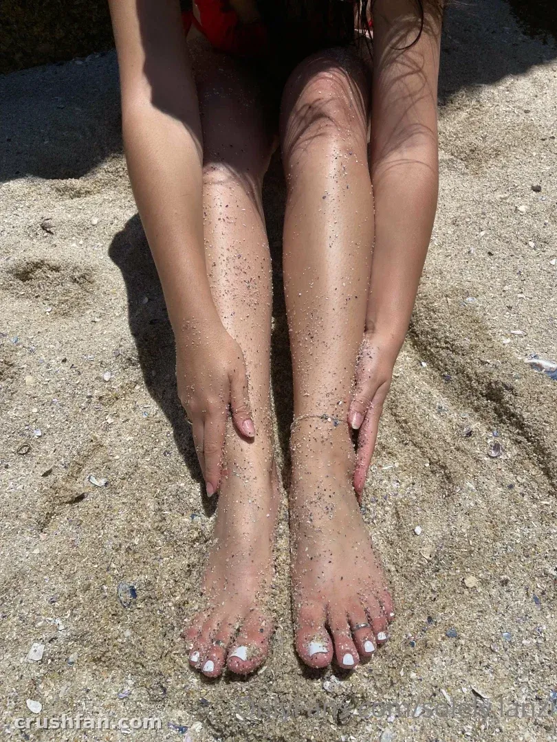 Lanzi sitzt auf sandigem Strand mit ausgestreckten Beinen und Sand auf ihrer Haut