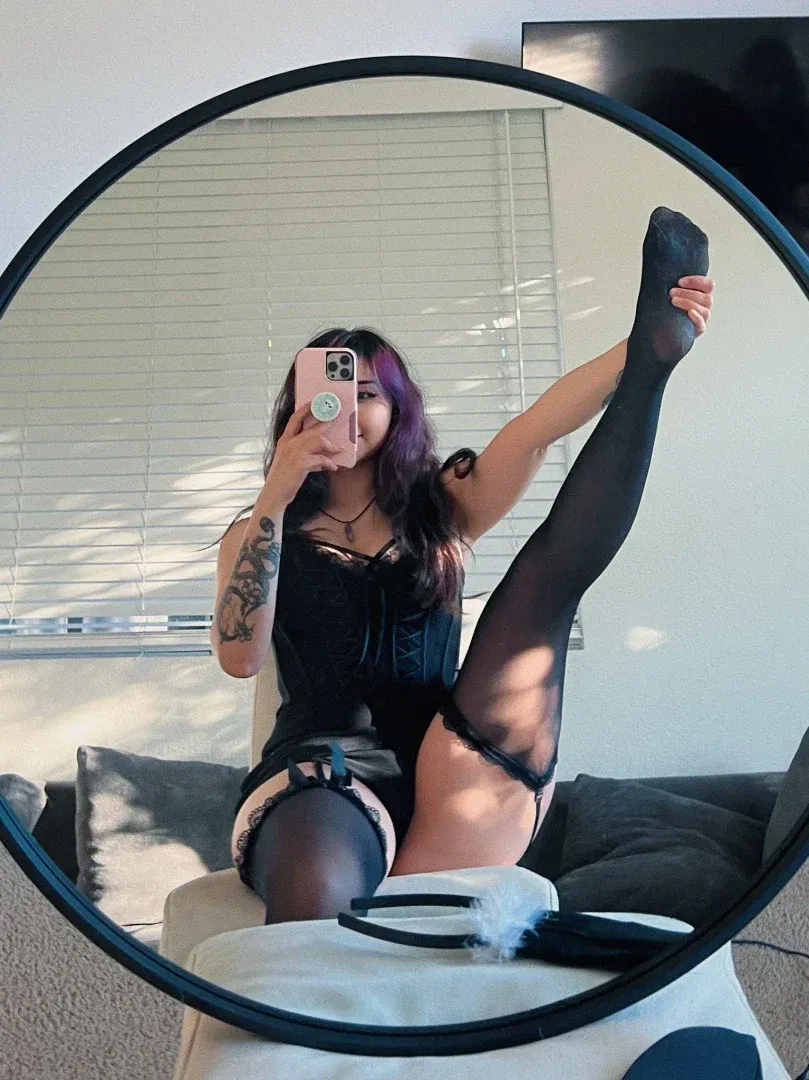 Jade tomándose un selfie frente al espejo en lencería negra y medias