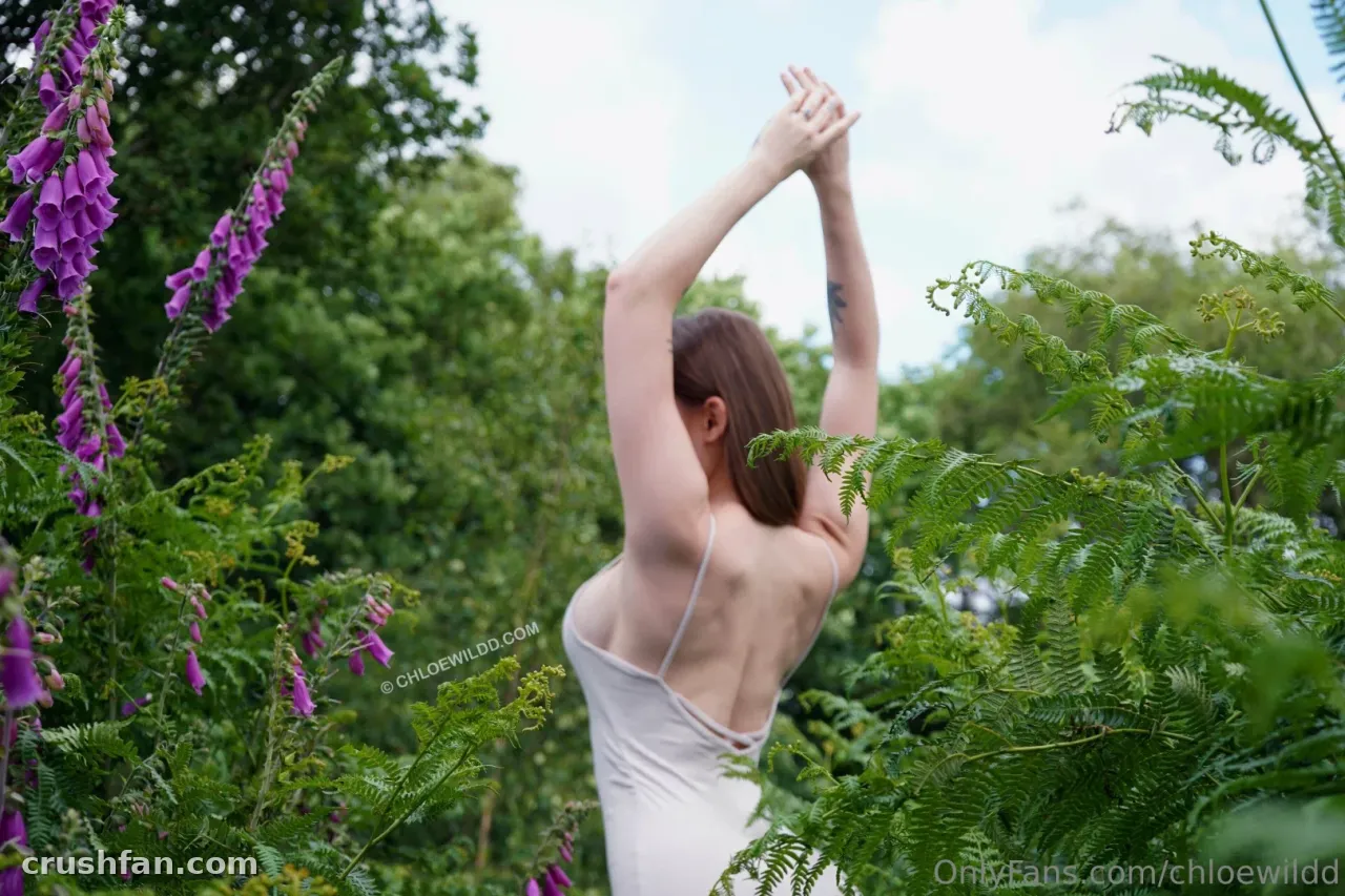 Chloe Wildd les bras levés parmi les digitales et les fougères dans un jardin