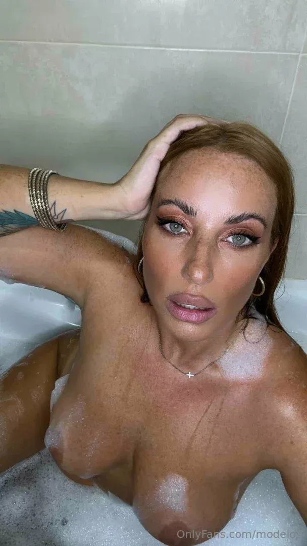 Modelos España in einem Schaumbad mit nassen Haaren und Creolen, die Hand hinter dem Kopf ruhend.