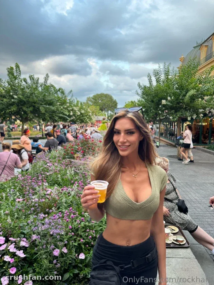 Holly Roxx smiling in a garden holding a drink among flowers and trees