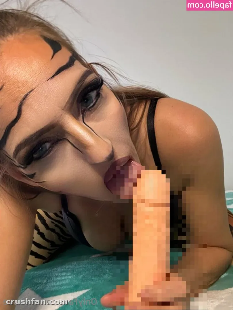 Close-up of LUSILOVE with black tiger-stripe face paint, wearing a black top on teal bedding