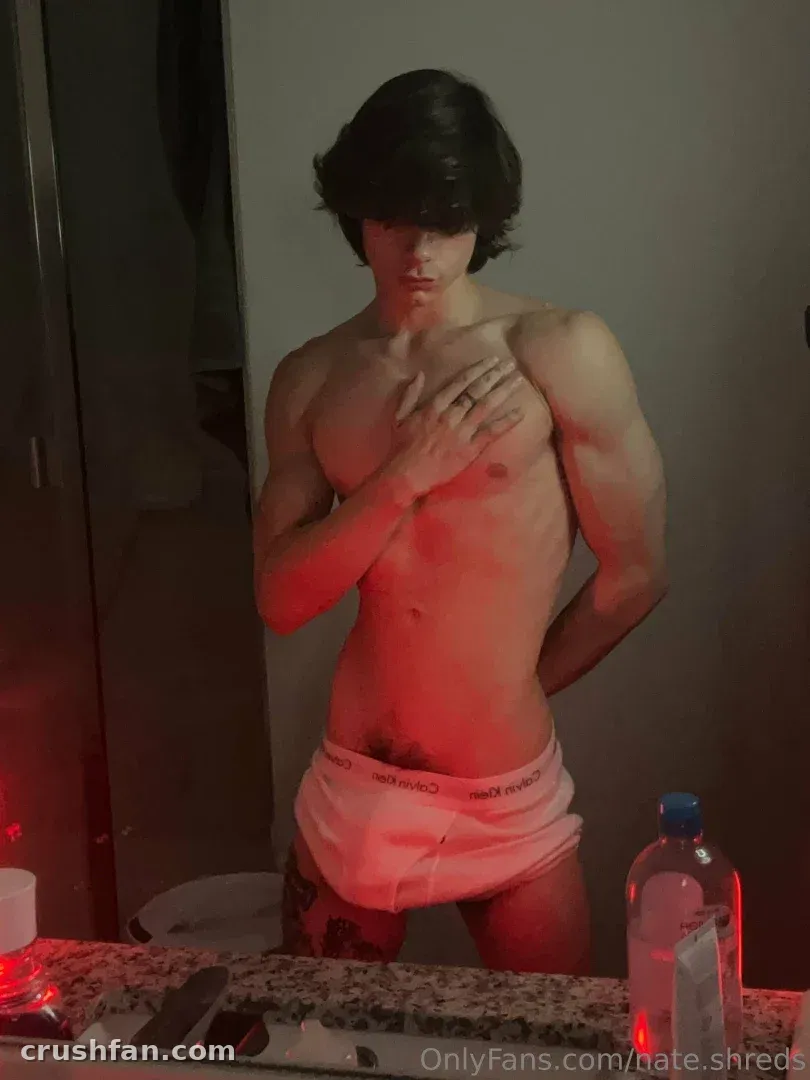 Shirtless man with dark hair posing in a red-lit mirror selfie