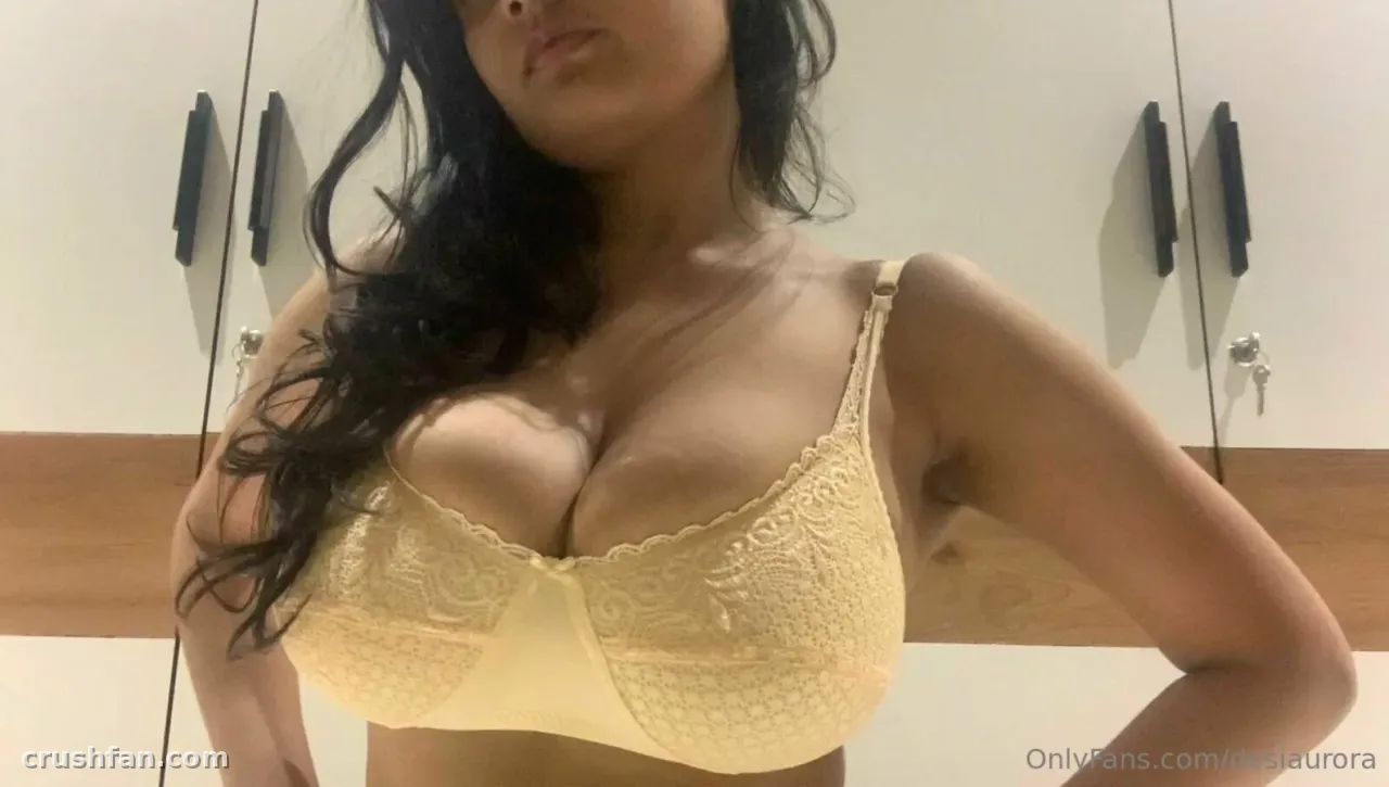 Desi Aurora in a pale yellow lace bra taking a mirror selfie in a bright room