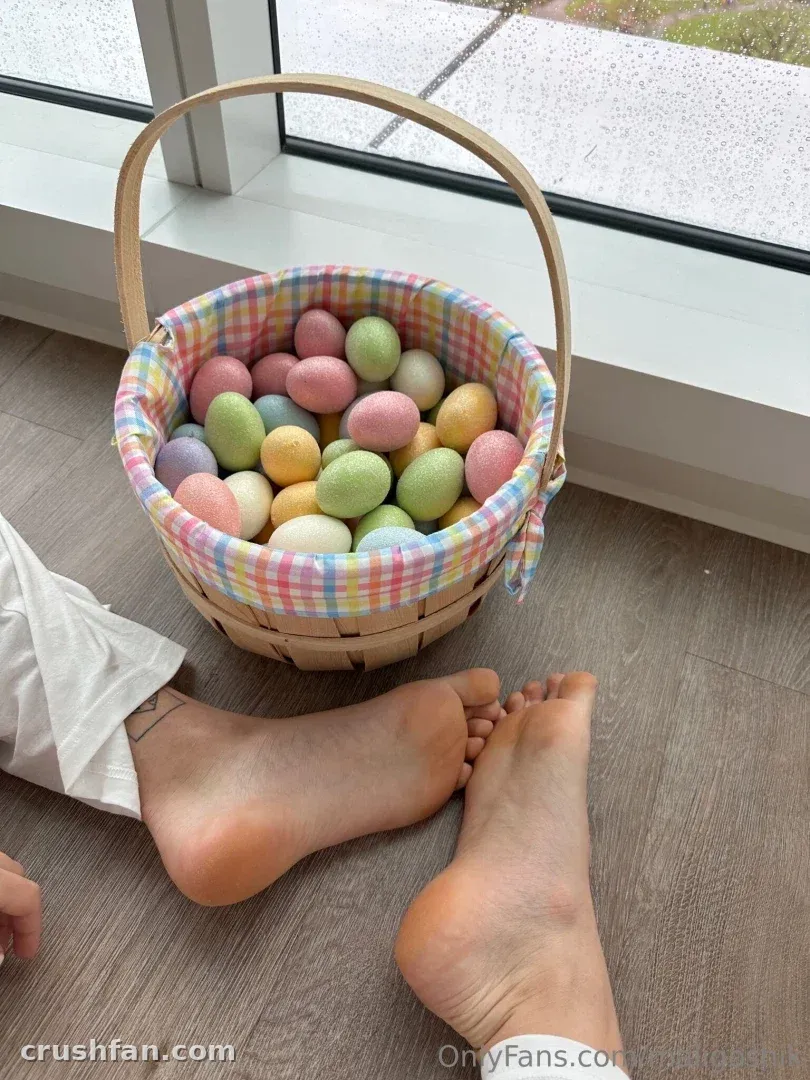 Bare feet beside a woven basket filled with pastel Easter eggs on a wooden floor