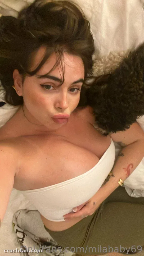 Mila ☆ Baby con un top blanco de hombros descubiertos tumbada en una cama en una selfie cercana.