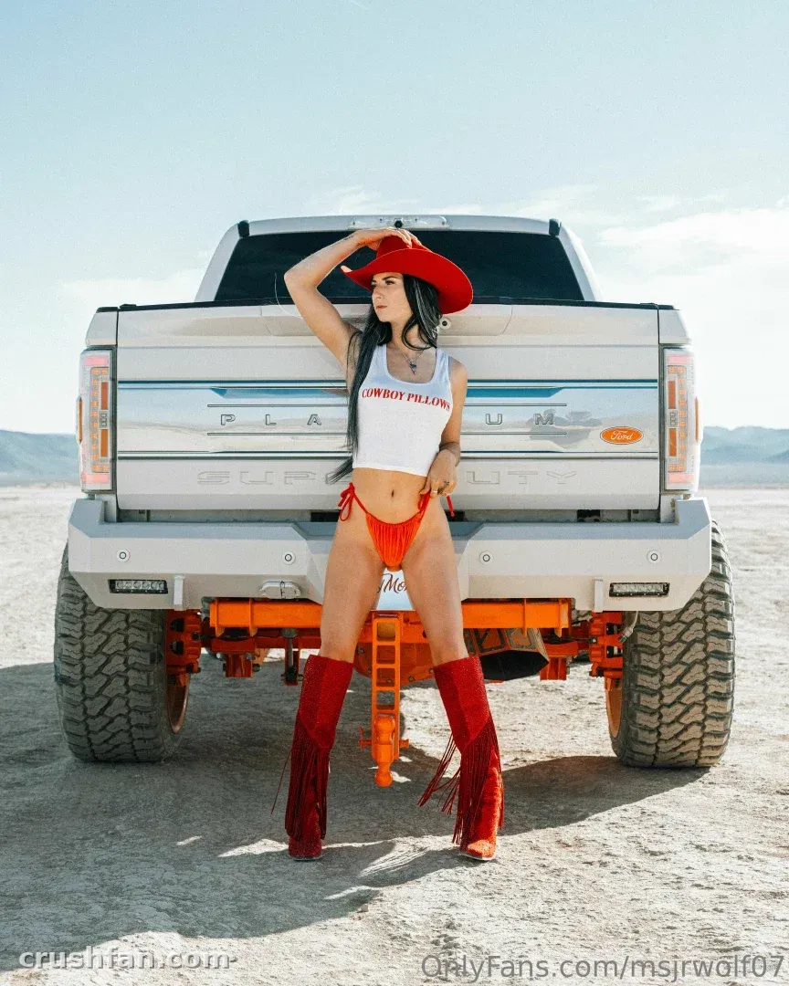 J in a red cowboy hat and boots posing by a white pickup truck in the desert