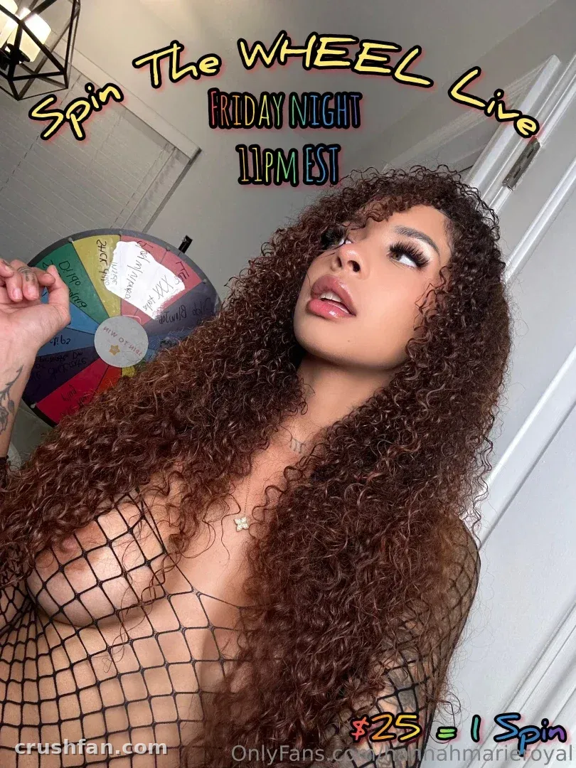 Creator with long curly hair in a black mesh top beside a colourful prize wheel indoors.