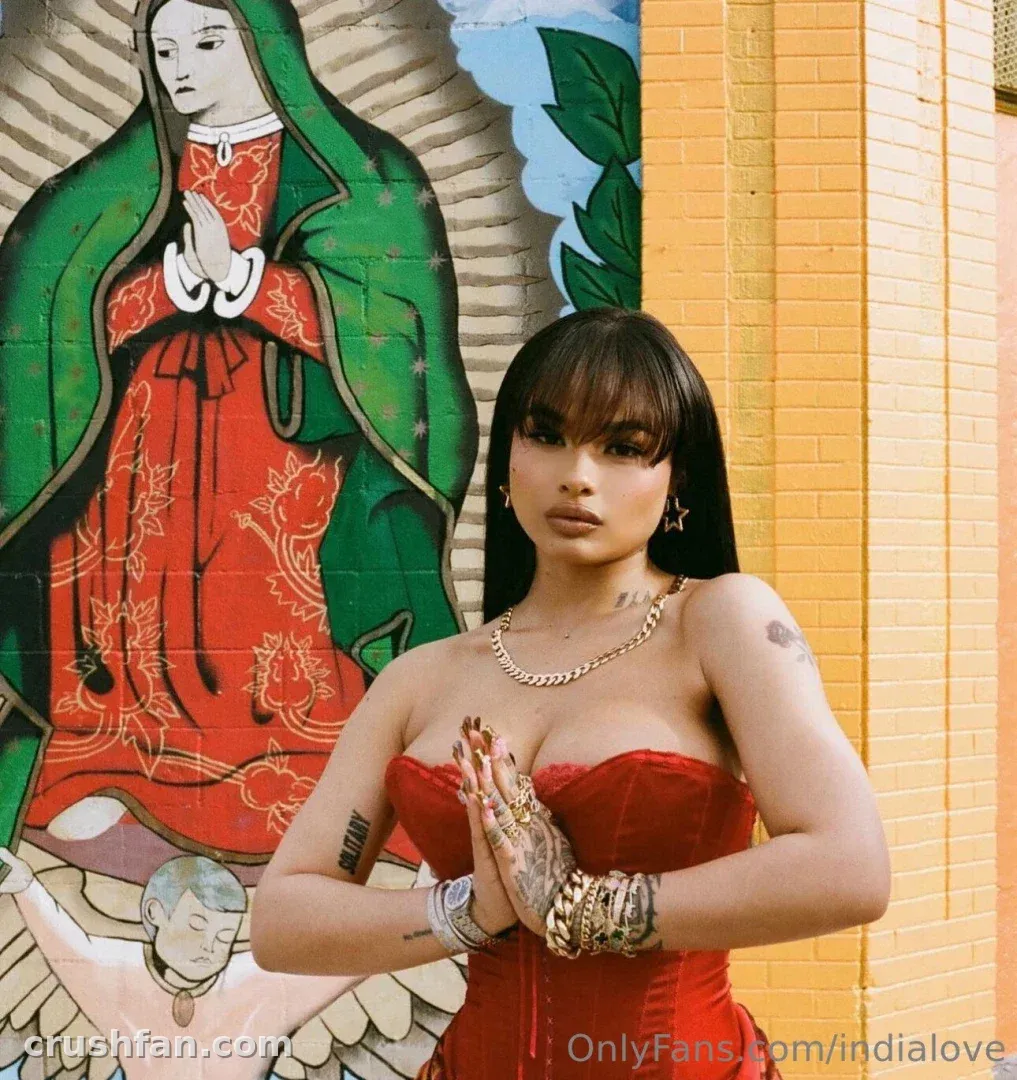India Love in a red dress with hands together in front of a colourful mural