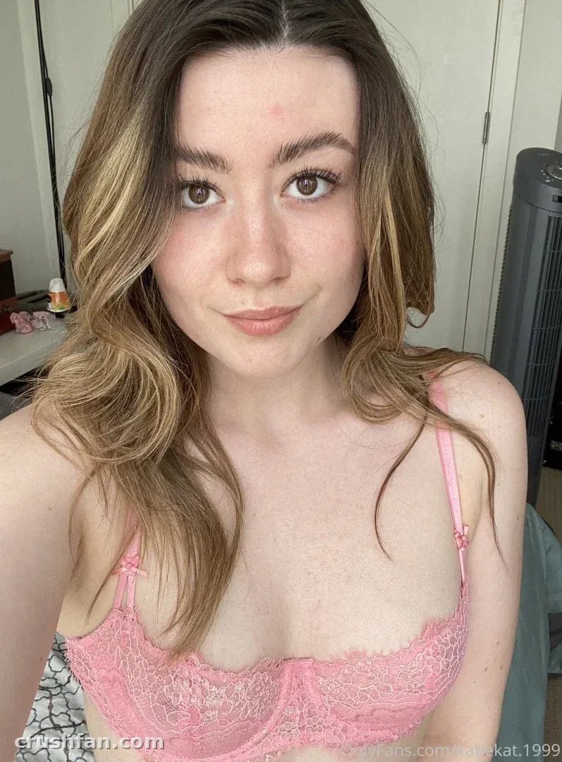 Katie Katrina se toma un selfie cercano con una blusa de encaje rosa en una habitación con luz suave