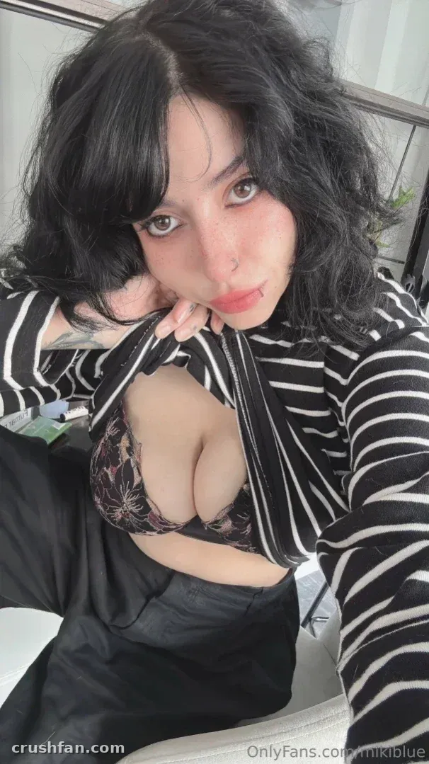 Miki Blue con un top de rayas y bralette de encaje tomándose un selfie en interiores