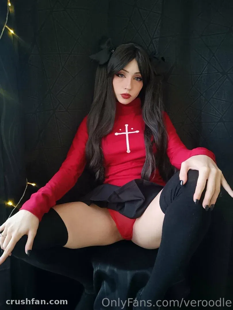 Creator in a red cross top, black skirt and stockings seated against a dark backdrop
