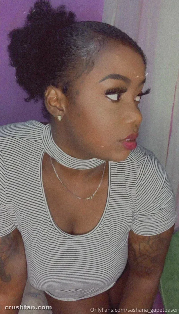 Sashiboo93 dans un haut choker rayé posant à l'intérieur près d'un mur violet.