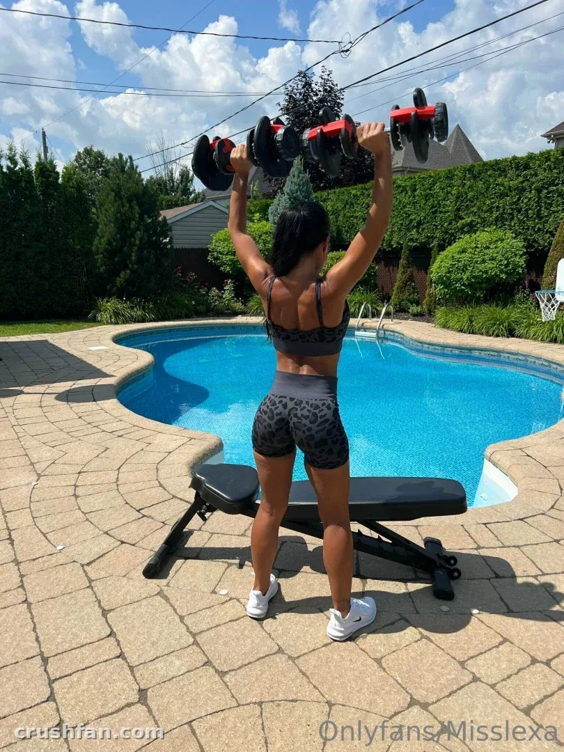 Miss Lexa levantando mancuernas por encima de la cabeza en un patio junto a una piscina