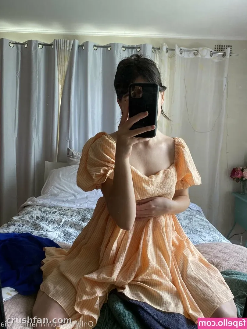 Creator in a peach dress taking a mirror selfie in a bright bedroom