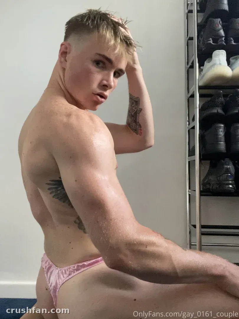 Shirtless creator in pink briefs glancing back beside a sneaker rack indoors