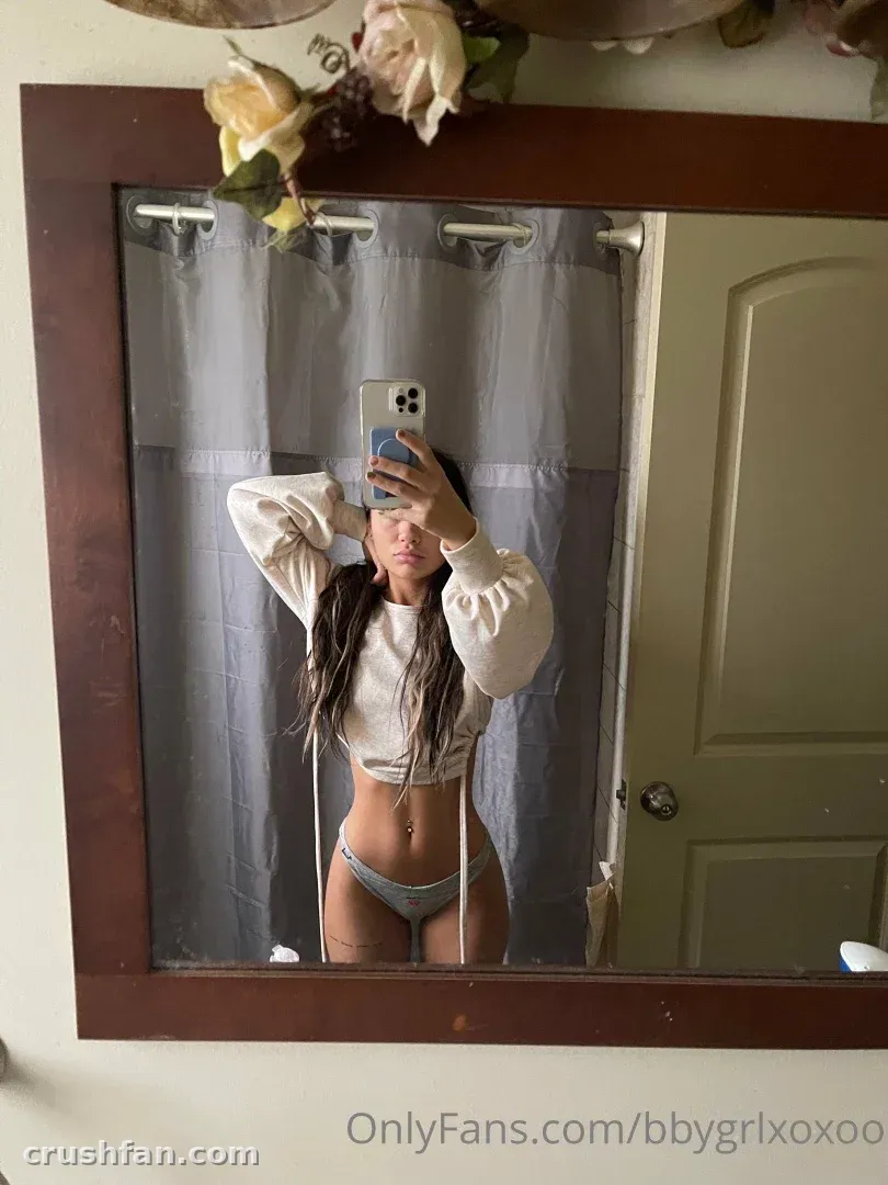 Babyyber in a white cropped sweater taking a mirror selfie indoors