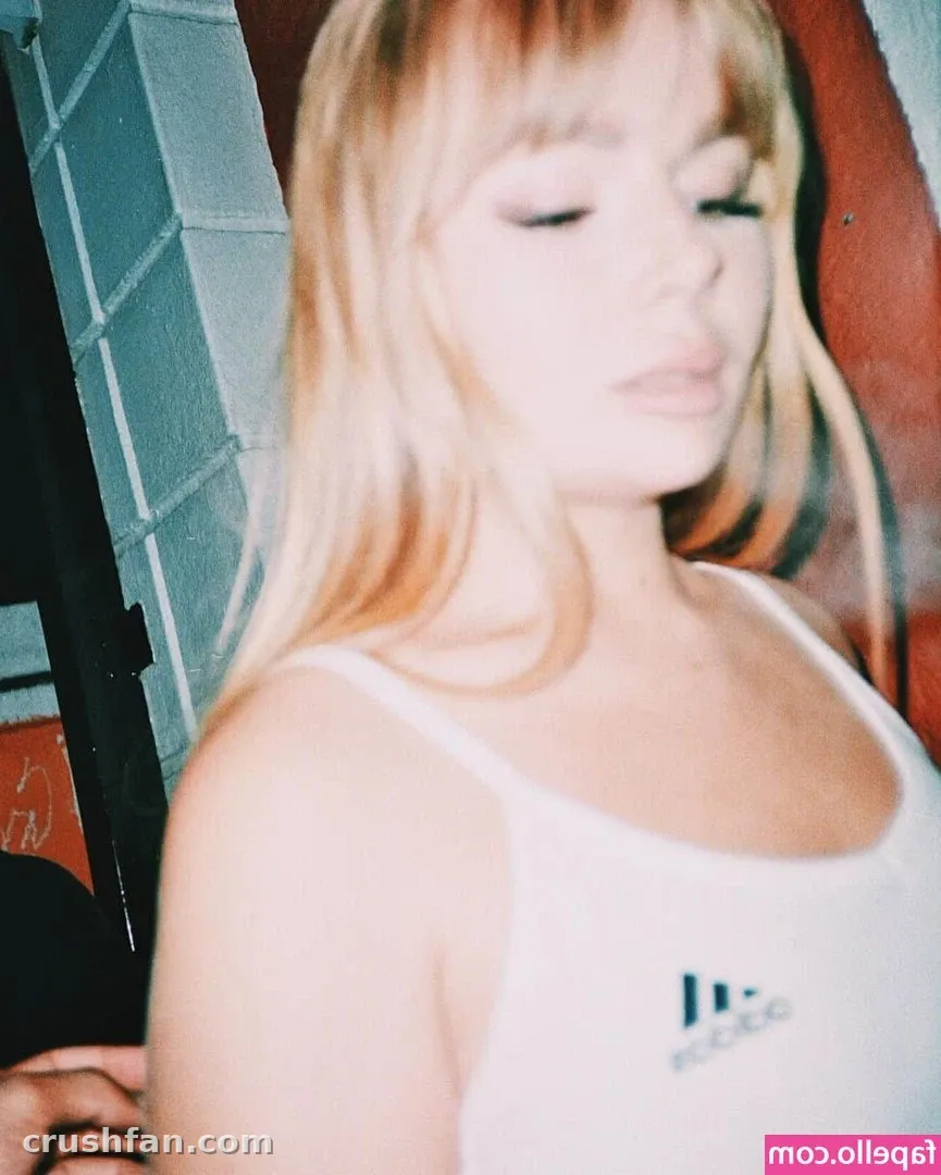 Emma Christina con los ojos cerrados y una camiseta sin mangas blanca frente a una pared de azulejos