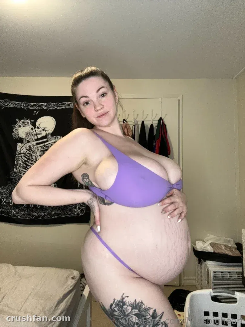 Lyla in a lavender two-piece set posing in a bedroom with a dark wall hanging behind her.