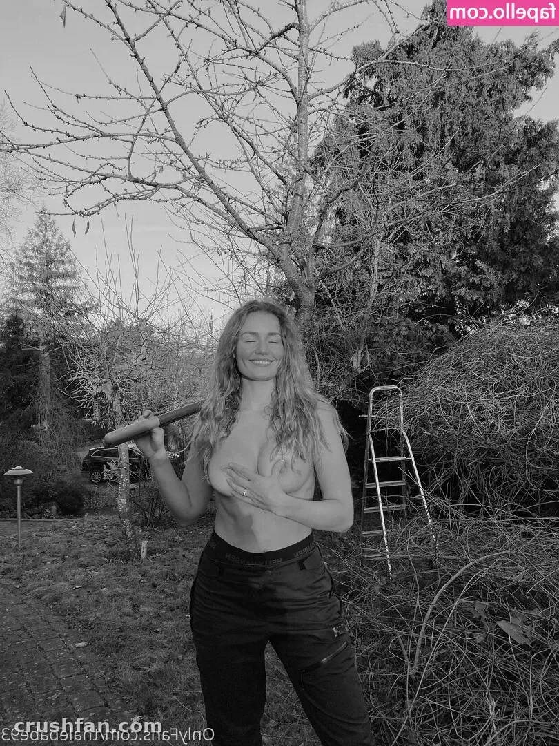 Black-and-white outdoor portrait of a smiling woman in dark trousers holding a tool handle
