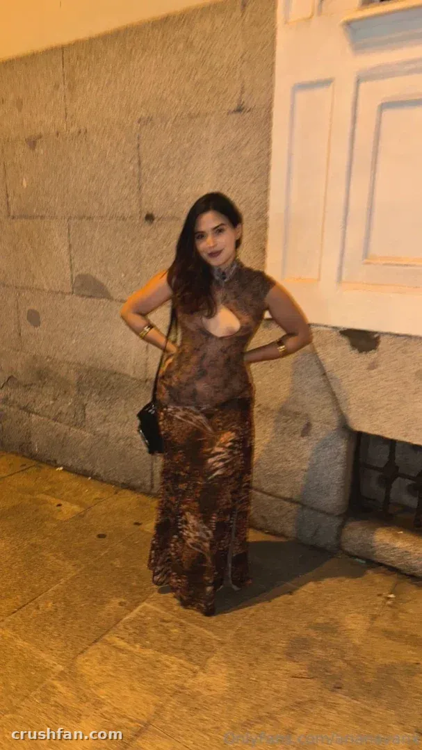 Mujer con un largo vestido transparente estampado de pie en una calle de piedra por la noche