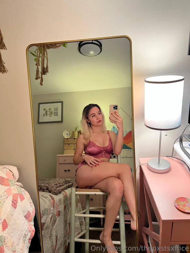 Maizie in rosa Dessous, die in einem Schlafzimmer ein Spiegel-Selfie macht