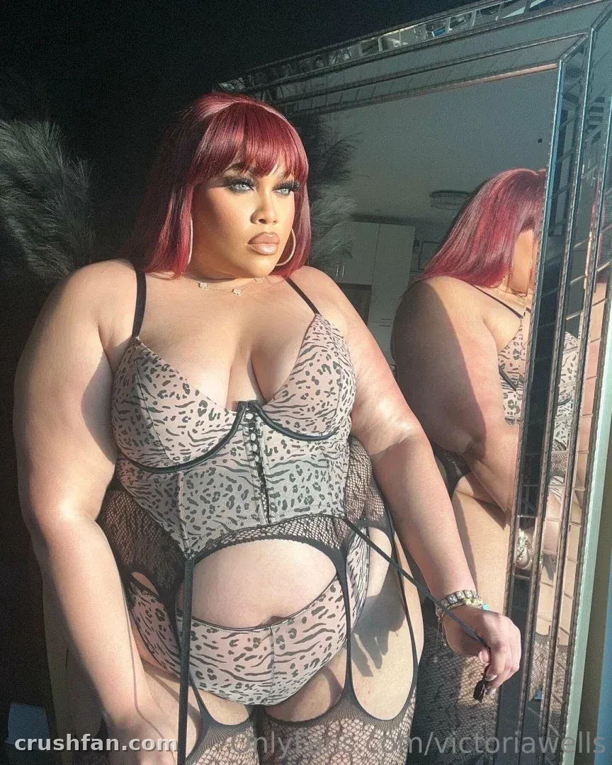 Victoria Wells con lencería estampada de leopardo de pie junto a un gran espejo a la luz del día