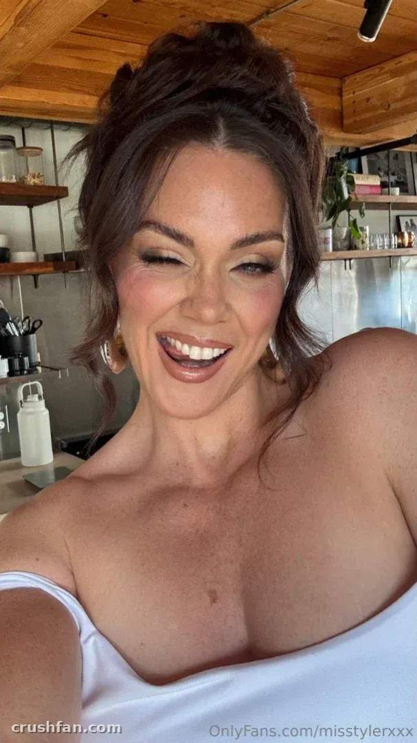 Alison Tyler laughing in a close-up indoor selfie, wearing a white off-shoulder top.