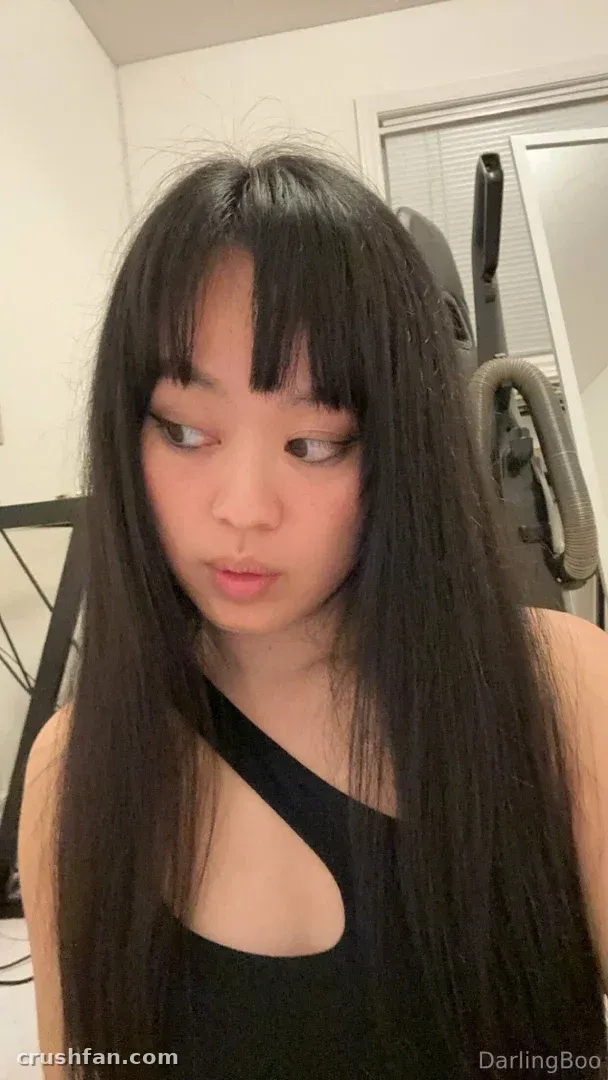 Darling Boo con el pelo largo y oscuro y flequillo, llevando una blusa negra recortada en interiores
