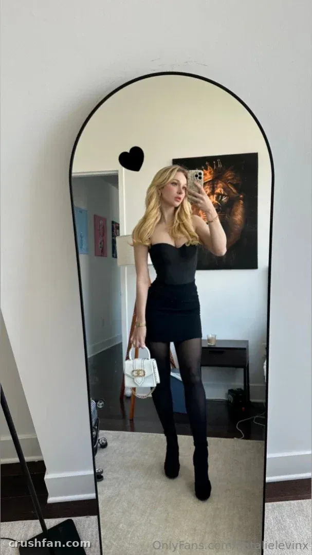Natalie in a black dress taking a mirror selfie in a bright room