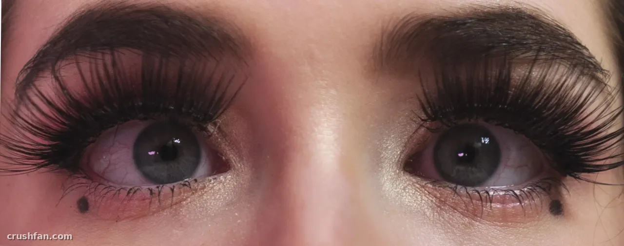Gros plan des yeux gris d'une femme avec de longs cils sombres et un maquillage doux.