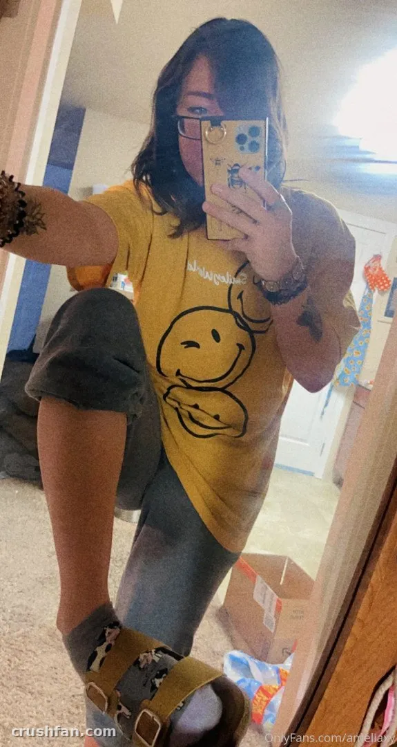 Amelia in a yellow graphic tee and rolled trousers taking a mirror selfie indoors