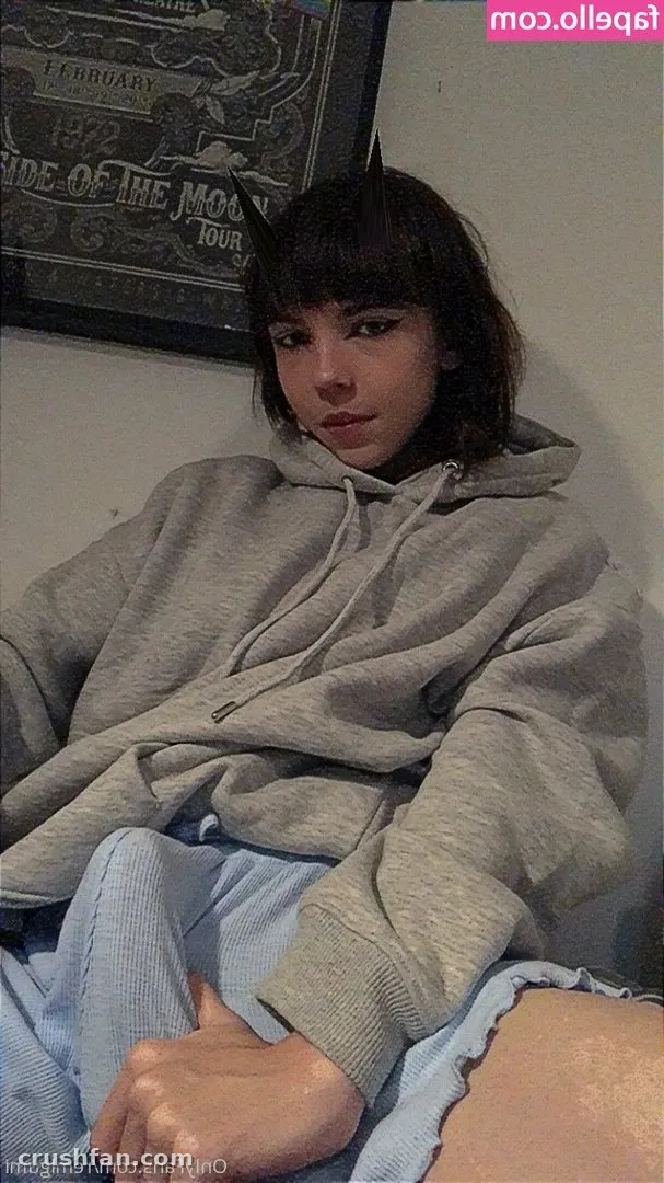 Remi in a grey hoodie and light blue trousers seated indoors in front of a framed poster