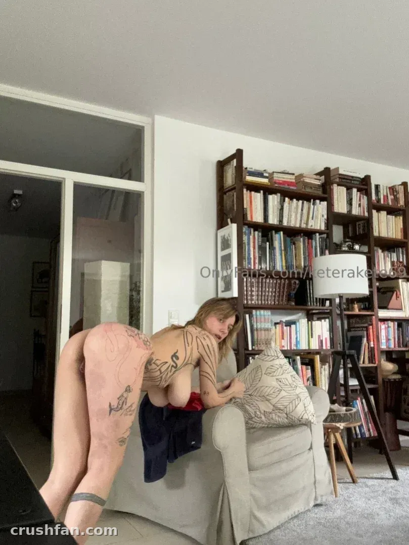 KAT inclinada sobre el brazo de un sofá en un salón con una estantería alta detrás