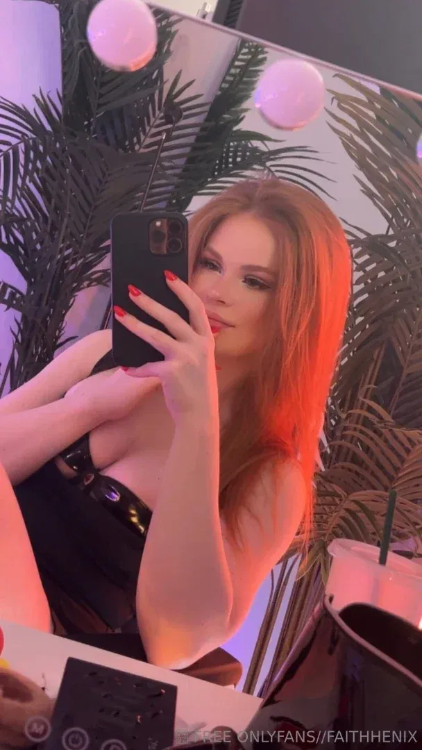 Faith takes a mirror selfie in a room with pink lights and palm leaves.
