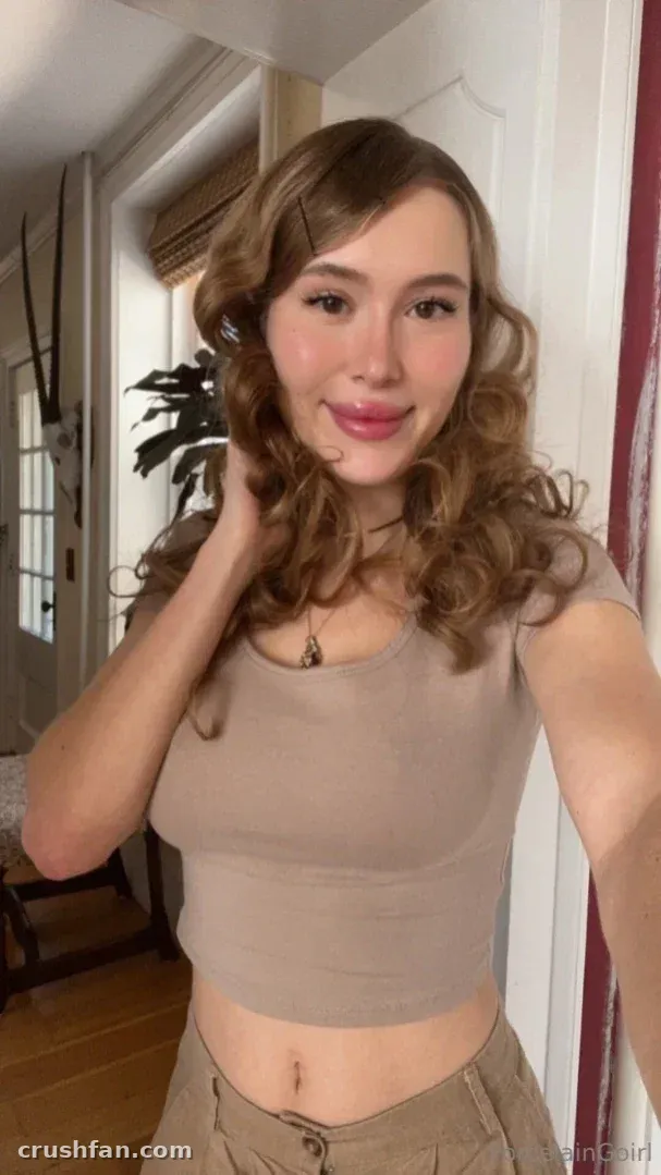 Rosealine in a beige cropped top indoors, hand near her neck