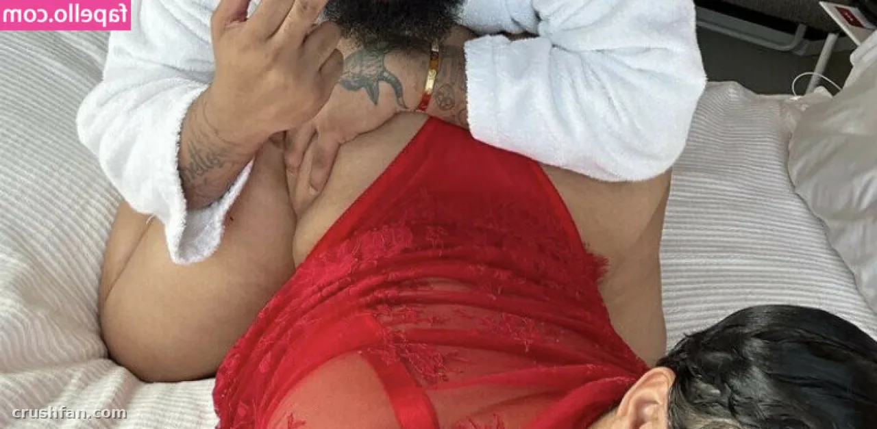 Criadora em um body de renda vermelho e roupão branco deitada sobre roupa de cama branca, vista de cima